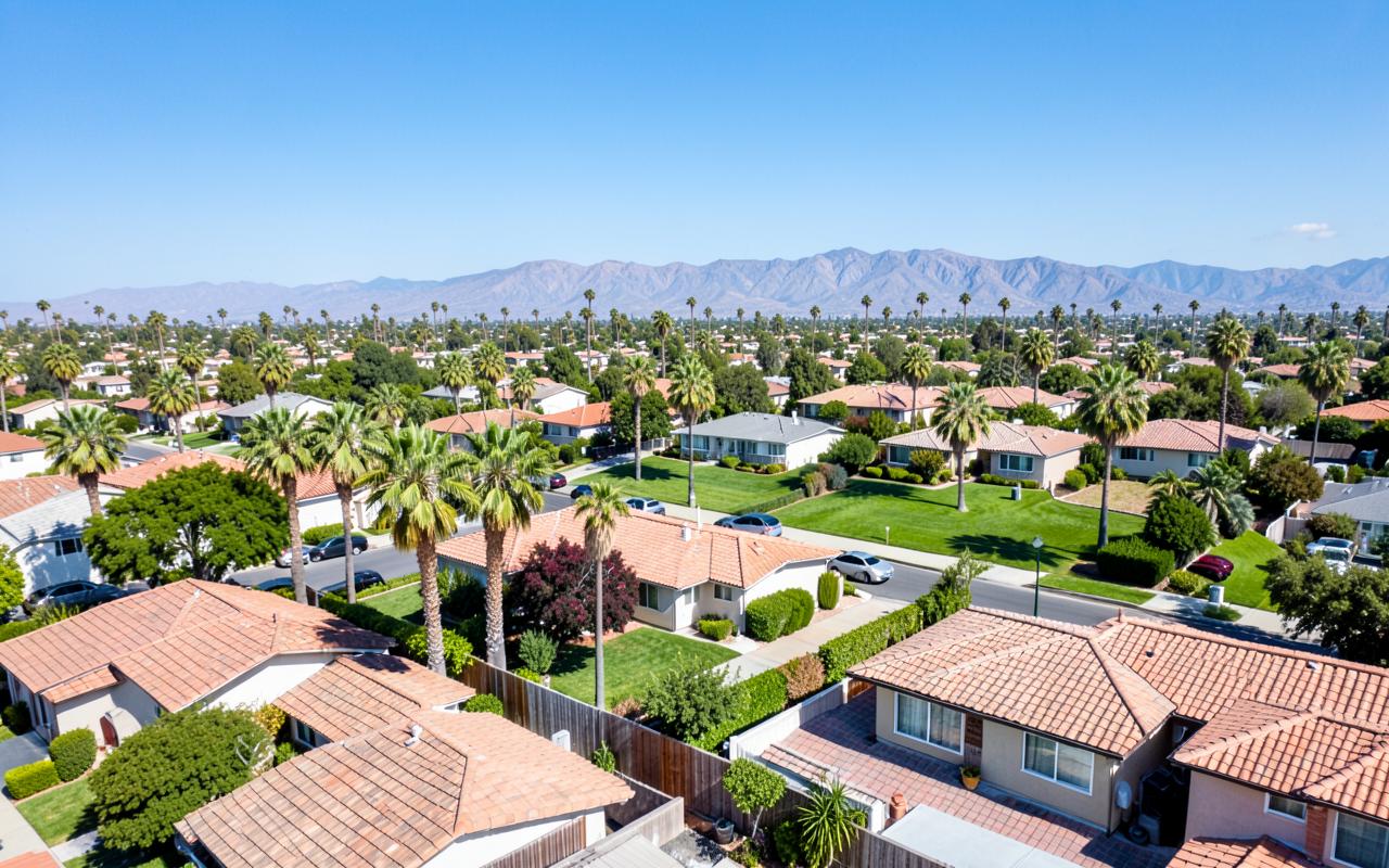 Sunny daytime aerial view of a Southern California residential neighborhood with palm trees and mountains behind