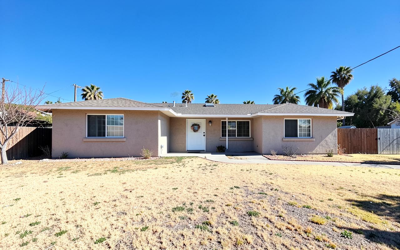 Empty single-story California stucco house in bright daylight with a dry lawn